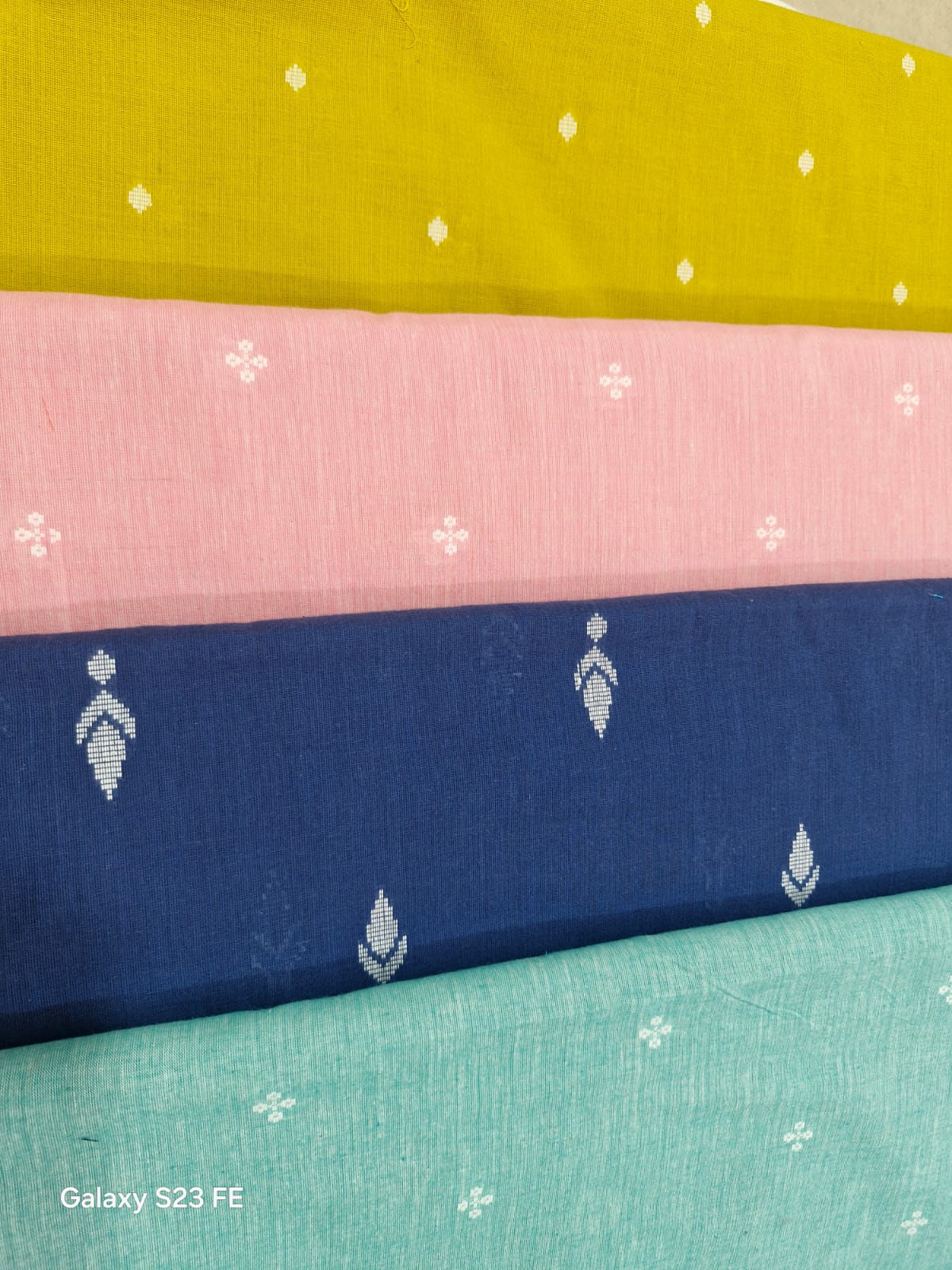 Stack of Mangalgiri cotton buti fabrics in yellow, pink, blue and teal