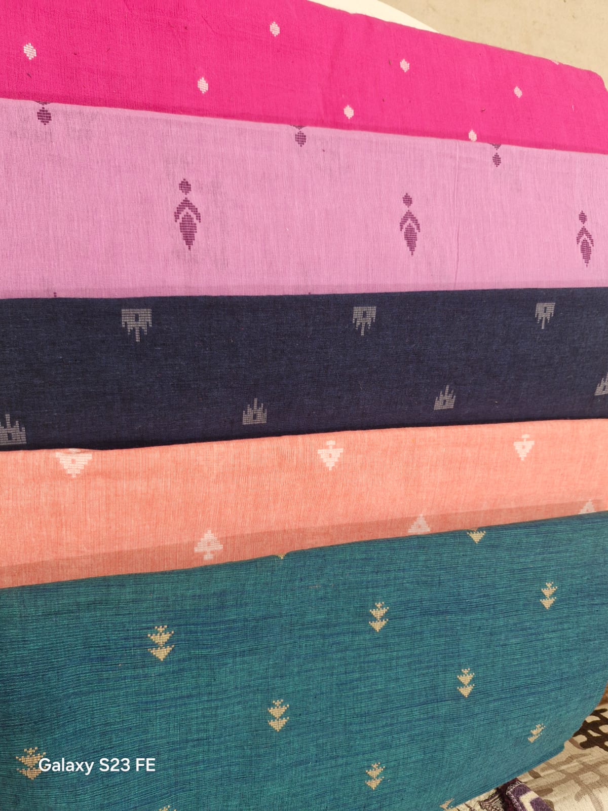 Stack of cotton buti dress fabrics in pink, navy, peach and teal